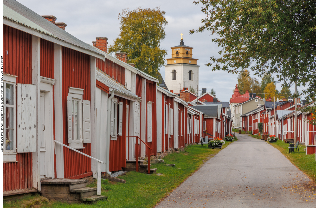 Die Siedlung ist eine Kirchstadt. Viele Kirchstädte in Nordschweden sind leider abgerissen, aber an einigen Orten gibt es sie noch. Schweden ist sehr dünn besiedelt, vor allem hoch oben im Norden. Wer zur Kirche gehen wollte (oder musste,
denn das war damals Pflicht), hatte oft große Wege zurückzulegen. Damit das machbar war, bauten sich die reicheren Bauern kleine Häuschen und Stallungen um die Kirche herum. So konnten sie dort übernachten, den Gottesdienst besuchen
und sich anschließend auf den langen Weg nach Hause machen.