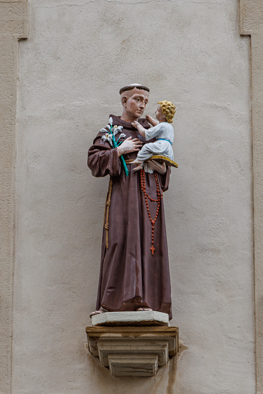 Diese polychrome Statue stellt den heiligen Antonius von Padua mit dem Jesuskind dar. Die Figur ist typischerweise in franziskanischer Kutte gekleidet und h&auml;lt Lilien sowie ein Buch. Solche Darstellungen sind im Historismus des 19. Jahrhunderts popul&auml;r geworden.