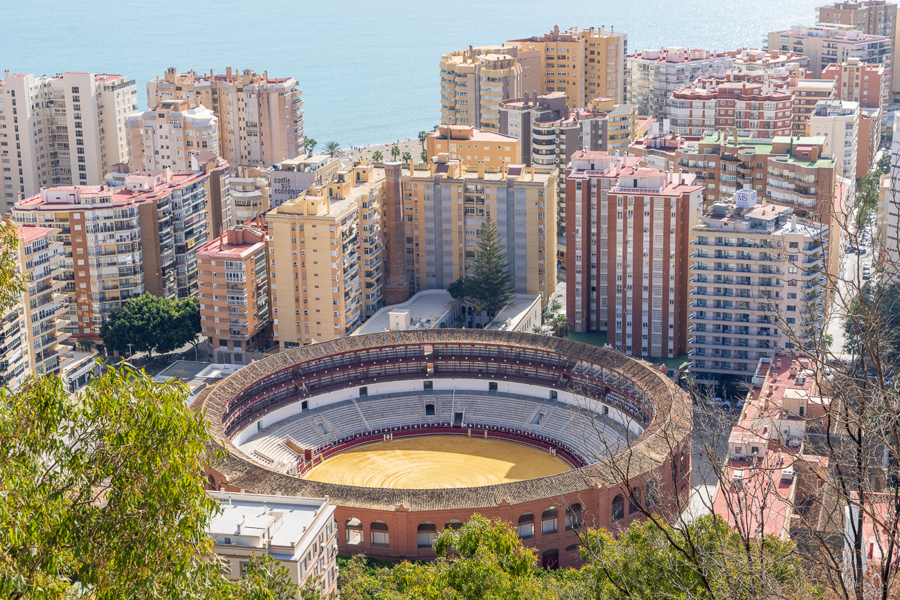 Blick von der Festung Alcazaba auf die imposante Stierkampfarena von Málaga. Sie befindet sich an der Paseo de Reding im Stadtviertel La Malagueta in der Nähe des Strandes inmitten moderner Hochhäuser. In der rund 50 Meter Durchmesser großen Arena ist Platz für nahezu 9.000 Menschen.Die Arena beherbergt zudem das von dem Architekten Joaquin Rucobo entworfene Musem „Museo Tarino Antonio Ordoñes“, benannt nach dem legendären Torero Antonio Ordoñes, der 1932 in Ronda geboren wurde. Er war einst der beste Torero Spaniens und trug auch in der Stierkampfarena von Málaga zahlreiche Siege davon. Antonio Ordoñes begegnete in seinem Leben mehr als 3.000 Stieren.
